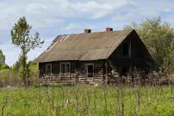 Obraz premium Ruins of a traditional village house. The old central residential architecture of Russia is destroyed and abandoned. Log cabin against a background of gray sky and green grass
