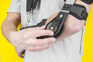 Man close up with a broken arm wearing in adjustable sling on yellow background