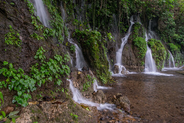 Many waterfalls going down a mountain surrounded by lush green tropical jungle vegetation. Long exposure shot. Seven Waterfalls, El Salvador.