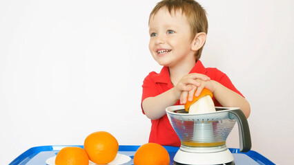 A happy baby boy squeezes orange juice with a juicer smiling and laughing