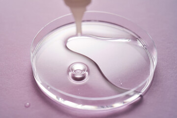 Serum or cosmetic oil flows into a transparent bowl on a purple background.