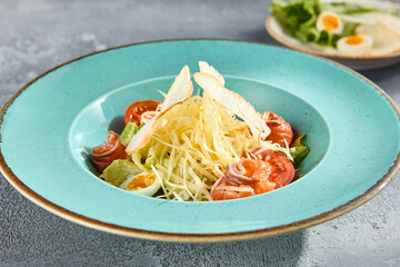Caesar salad with smoked salmon, cheese, and boiled eggs on a turquoise plate