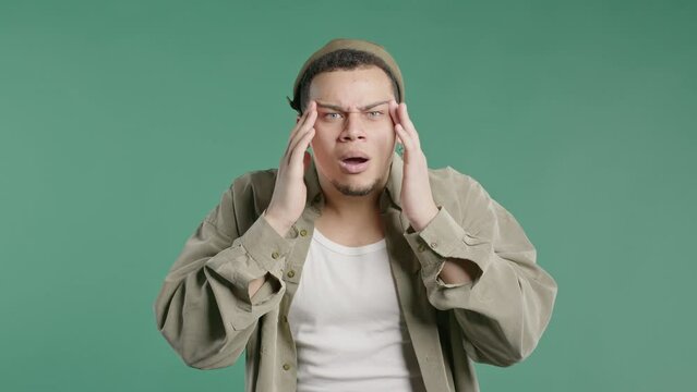 Young stylish man rubs eyes, peers more closely smiling to camera on green, wow