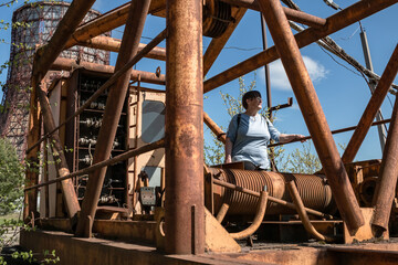 An elderly woman against the backdrop of a destroyed factory.