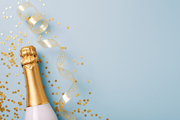 Flat lay, top view of laying champagne bottle with gold confetti on pastel blue background. Celebration of success, birthday, Christmas, New Year, wedding, party