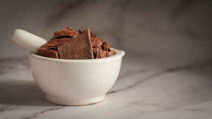 Close-up of Dry Organic Arjuna (Terminalia Arjuna) Barks, in white ceramic mortar and pestle, on a marble background.