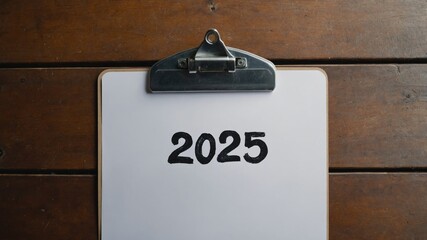 Clipboard on wooden table with year 2025 written on paper