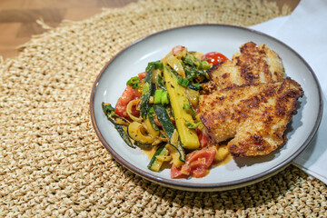 Crispy fried redfish fillet on Mediterranean vegetables such as zucchini, tomatoes and leek, on a gray plate and a placemat of natural fibers, healthy meal for low carb diet, copy space