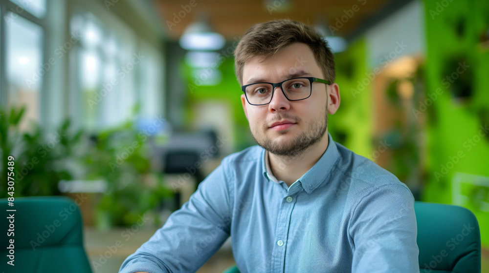 Canvas Prints A man wearing glasses and a blue shirt sits in a green chair. He is looking directly at the camera. brutal handsome young man of European type, average man with broad shoulders