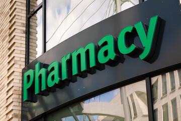 Obraz premium Pharmacy logo sign on a building facade. Drugstore advertisement in big green colored letters. Retailer for pharmaceuticals and medicine in a European city.