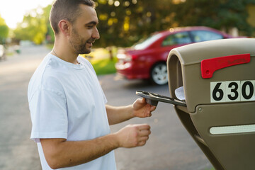 Young home owner checks on new letters and bills in his american typical mailbox on sunny warm...