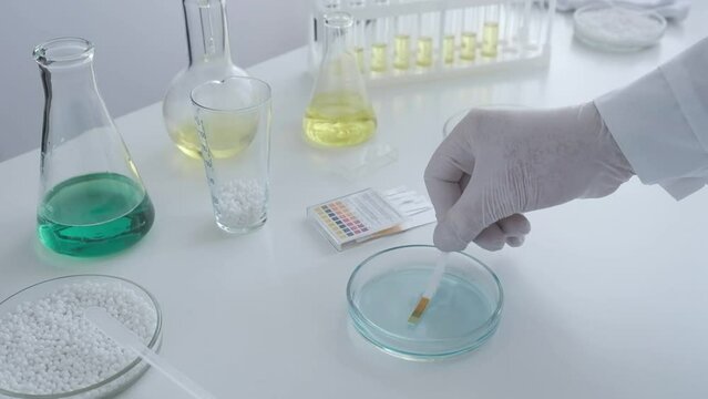A scientist in a chemical laboratory takes measurements of the acid-base balance of a liquid in a Petri dish.