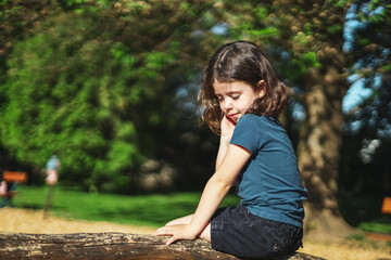 Portrait of a caucasian beautiful girl sits half-side on a wooden pole in a park