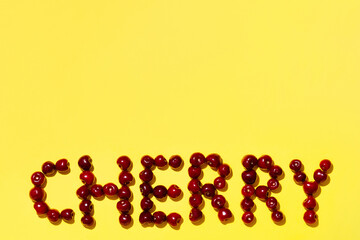 The inscription "cherry" made of ripe cherries on a yellow background. Top view. Space for text.