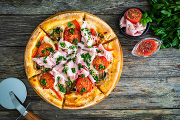 Pizza with cooked ham, mozzarella cheese and vegetables on wooden table
