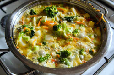 A boiling pot of vegetable soup with carrot, broccoli on top of the stove.