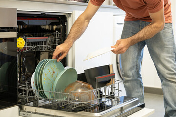 young man putting a dishwasher in his house after a meal. Man doing housework.