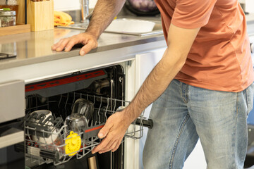 young man putting a dishwasher in his house after a meal. Man doing housework.