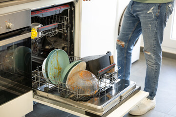 young man putting a dishwasher in his house after a meal. Man doing housework.