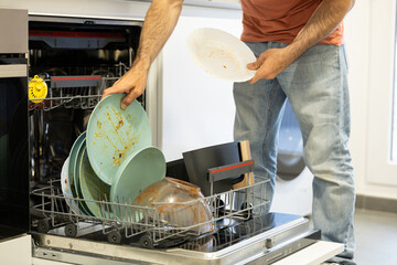 young man putting a dishwasher in his house after a meal. Man doing housework.