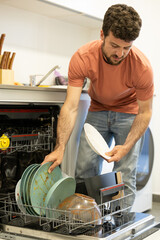 young man putting a dishwasher in his house after a meal. Man doing housework.