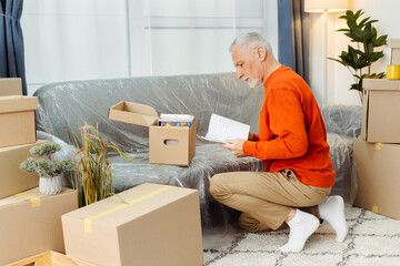 Senior man examining belongings while unpacking cupboard boxes at new apartment