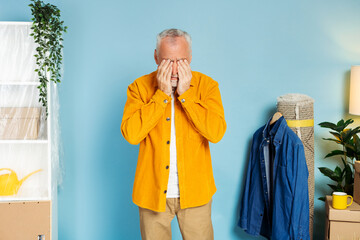 Exhausted senior mature old man rubbing eyes at home full of cupboard boxes