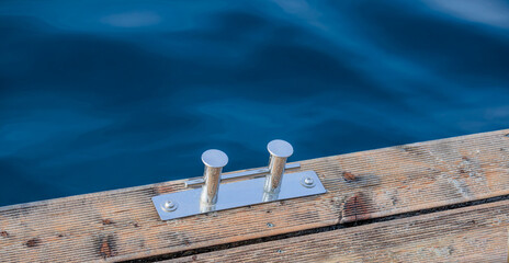 Metal mount for mooring boats (stainless steel  bollard) on a wooden platform near a body of water.