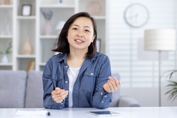 Asian woman engaging in a video call, chatting and communicating from a modern living room setting.