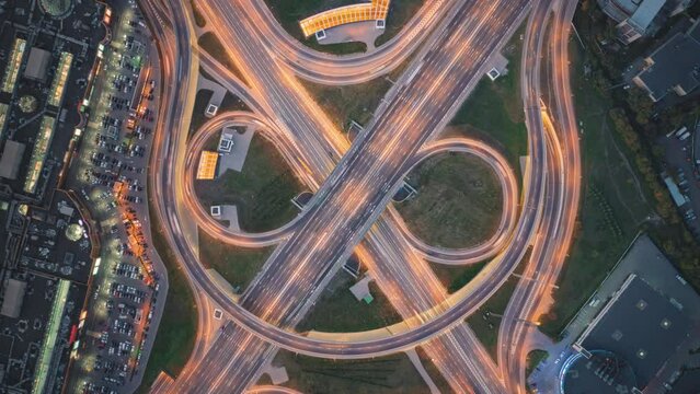 Top-down time-lapse, camera moves up and rotates over fast-moving cars at rush hour on a city crossroad. Intense traffic at a modern, multi-level intersection with beautifully moving vehicles.