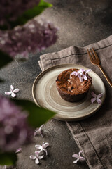 Fresh homemade chocolate muffin close up on a rustic plate with lilac flowers