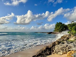 view of a seaside of guadeloupe with a small sandy beach and rocks with some clouds in the sky
