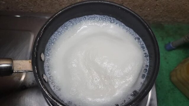 boiling milk on a gas stove boiling milk in a saucepan on the stove and flows. Milk boils and steams hot. Boiling milk in a stainless steel vessel. 4K Footage