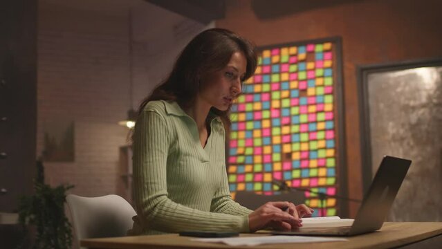 Footage of elegant attractive young Caucasian woman in mint clothes typing on keyboard and looking at screen of laptop. Female student studing economics. Girl preparing for exams and taking notes