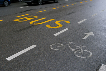 A paved city street with yellow markings designating a bus lane and white markings designating a...