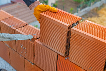 Worker builds a brick wall for house construction. Worker building a brick wall using mortar. Close-up of bricklayer placing bricks at construction site. Labourer with bricks.