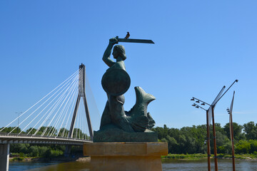 Warsaw, Poland. Statue of Mermaid (Polish: Warszawska Syrenka) symbol of Warsaw by the Vistula river on the background of Swietokrzyski Bridge. Spring time in Warsaw, Poland © PaulSat