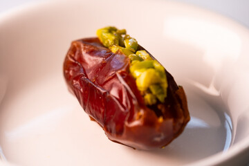 detail of a white porcelain plate with a magnificent and large fresh Dubai date filled with pieces of chopped pistachio with honey