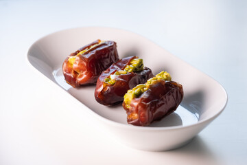 a white porcelain platter with magnificent large fresh Dubai dates filled with pieces of chopped pistachio with honey