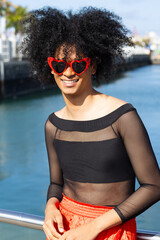 Non-binary person with afro hair and heart-shaped sunglasses, looking at the camera while smiling.