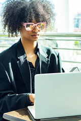 Non-binary executive, wearing a black suit and oversized sunglasses, working with their white laptop