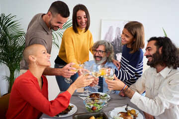 Happy Caucasian people toasting with white wine at a meal at home. Smiling family of diverse generations together around the table at festive event at weekend. Domestic life celebration 