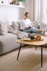 Coffee table with tea cup and croissant against blurred background with woman reading book