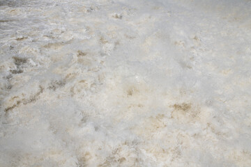Background and close-up of roaring brown water that flows rushing and forms small whirlpools.