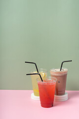 Three takeaway glasses of colourful summer drinks. Lemonades and cocktail on coloured background