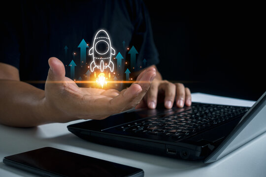 The concept of a startup business is technology adoption to scale existing business and organizational operations. Businessman use laptop with virtual screen of rocket icon and up arrow fast start up.
