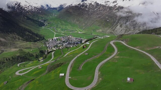 The alpine village of Andermatt surrounded by green meadows, and snowy peaks in the background, Canton of Uri, Switzerland, Europe