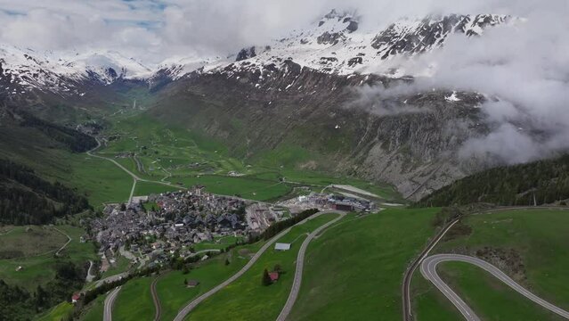 The alpine village of Andermatt surrounded by green meadows, and snowy peaks in the background, Canton of Uri, Switzerland, Europe