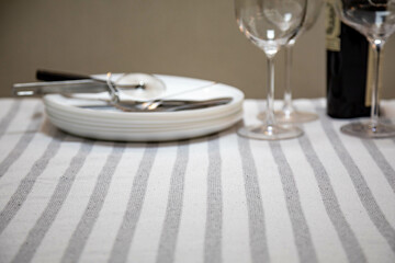 Table set neatly on a white striped tablecloth, bottle of wine, crystal glasses, white plates and cutlery