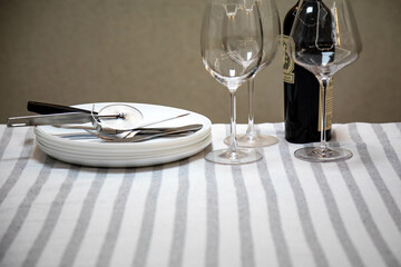 Table set neatly on a white striped tablecloth, bottle of wine, crystal glasses, white plates and cutlery